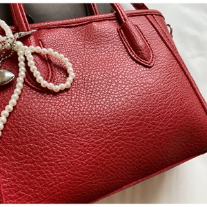 Close-up of red lychee grain leather tote bag with white pearl and heart charms