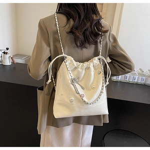 Detail of cream bucket backpack with pearl decor and silver bow charms on a model