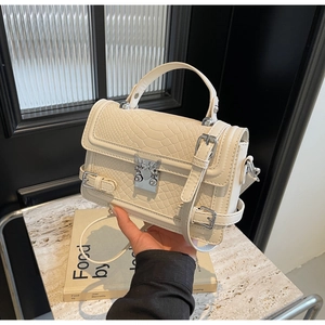 Close-up of beige crocodile-textured handbag featuring a unique silver heart lock