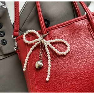 Detail of red litchi texture handbag with pearl bow charm and silver heart pendant
