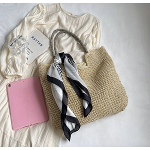 Flat lay of large straw tote bag with striped handles and decorative silk scarf detail