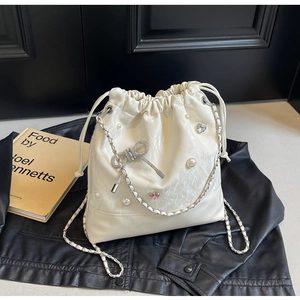 Detail of cream bucket bag with pearls, rhinestone bows, and silver chain straps