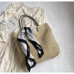 Detail of a beige woven straw tote bag featuring black and white striped rope handles