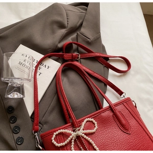 Detail of red tote bag with pearl bow decoration and lychee leather texture