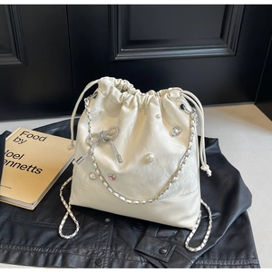 Close-up of cream bucket bag featuring pearl decor, diamond bow and silver chain strap