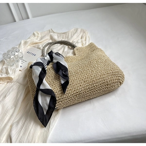 Detail of beige straw tote bag with woven texture and striped handles with scarf