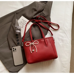 Close-up of red litchi texture handbag featuring pearl bow and heart pendant detail