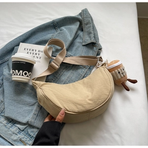 Beige canvas crescent crossbody bag with plush coffee cup charm on casual denim background