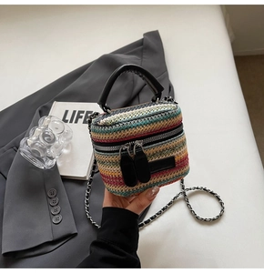 Detail of colorful woven straw mini bag with black leather handle and silver chain strap