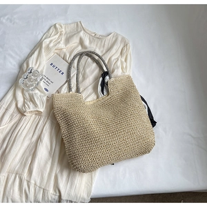 Detail of beige straw tote bag featuring black and white striped rope handles and silk scarf
