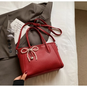 Detail of red litchi texture handbag with pearl bow pendant and adjustable strap