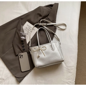 Detail of silver lychee pattern handbag with pearl bow and heart charm on blazer