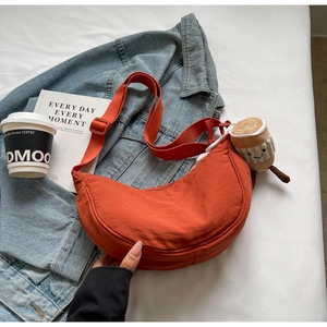 Orange crescent canvas crossbody bag with coffee plush pendant in urban setting