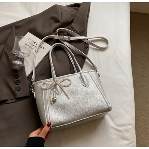 Detail of silver crossbody bag featuring a pearl bow charm and heart metal pendant