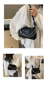 Detail of black crocodile texture shoulder bag with silver chains and brand lettering