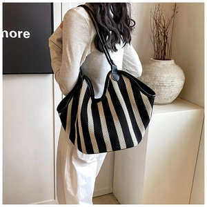 Detalle de bolso tote de rayas con asas de cuero llevado por una modelo en un interior
