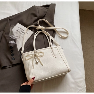 White textured leather tote with pearl bow and silver heart pendant on a blazer