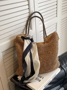 Brown hand-woven straw tote bag with striped scarf accessory on a leather sofa