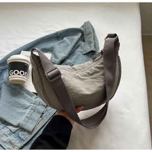 Détail du sac dumpling en nylon gris foncé avec bandoulière sur veste en jean bleue