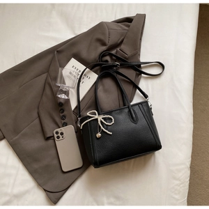Detail of black litchi texture leather tote bag with pearl bow charm on white bedding