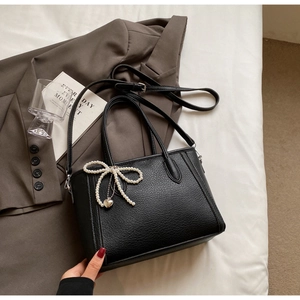 Detail of black lychee leather bag featuring pearl bow and golden heart charm