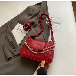 Detail of red crocodile texture bag with silver chain and braided handle on white desk