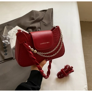 Detail of red croc-embossed handbag featuring a gold chain and woven strap texture