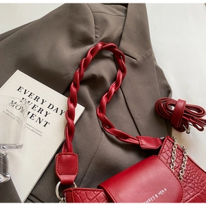 Detail of red croc-embossed leather bag with chain strap on dark blazer background