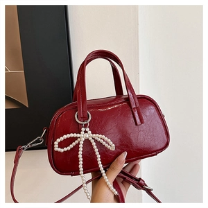Detail of burgundy wrinkled leather handbag with elegant pearl bow charm and top handle