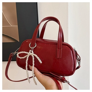 Close-up of dark red glossy patent leather handbag with a white pearl bow charm