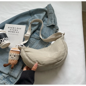 Détail du sac bandoulière demi-lune en nylon beige avec breloque tasse à café en peluche