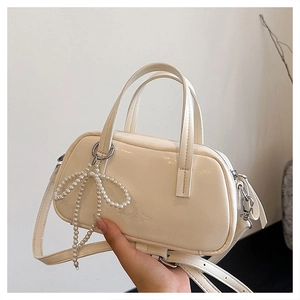 Detail of elegant cream handbag featuring a large pearl bow charm and silver hardware