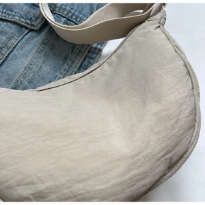 Détail du sac demi-lune en nylon beige clair avec texture lisse sur veste en jean