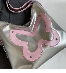 Close-up of silver tote bag featuring a pink butterfly patch with rivet detailing