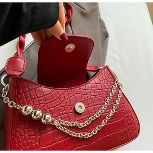 Close-up of red crocodile-embossed leather bag with silver chain and magnetic closure