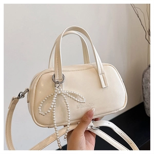 Close-up of cream square handbag with pearl bow charm and adjustable shoulder strap