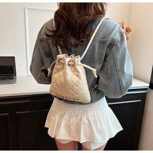 Quilted cream PU leather bucket backpack detail featuring metal letter branding and drawstring