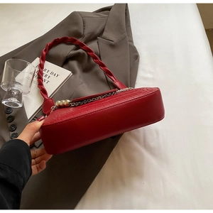 Detail of red crocodile texture handbag with woven handle and metal chain decoration