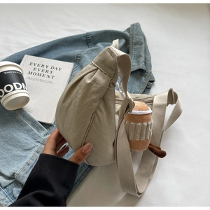 Gros plan d'un sac bandoulière en nylon beige avec breloque et sangle large