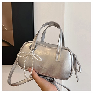 Detailed close-up of metallic silver bag with pleated texture and pearl bow charm