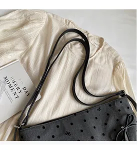 Detail of a grey polka dot canvas tote bag with slim black leather handles and bow embroidery