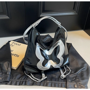 Detail of black glossy tote bag featuring a large silver butterfly and chain decoration