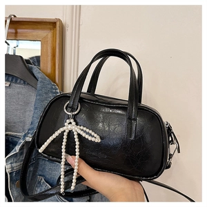 Detail of black glossy wrinkled leather handbag featuring a pearl bow charm and double handles