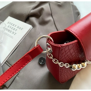 Detail of red crocodile textured handbag with silver ring buckle and chain strap