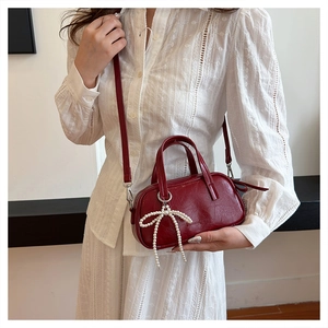Detail of burgundy leather mini bag featuring large white pearl bow accessory