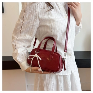 Detail of burgundy leatherette handbag featuring pearl bow charm and metal buckle straps