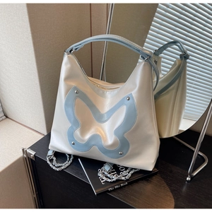 Detail of pearlescent white tote featuring a large blue butterfly patch and silver chain strap