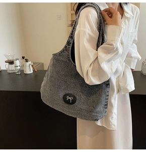 Détail du grand sac cabas en denim gris foncé avec écusson nœud noir élégant sur l'épaule