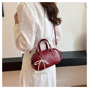 Detail of dark red leather textured mini handbag with elegant pearl bow charm