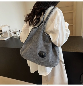 Détail d'un grand cabas en denim délavé gris porté épaule avec détail de nœud en métal